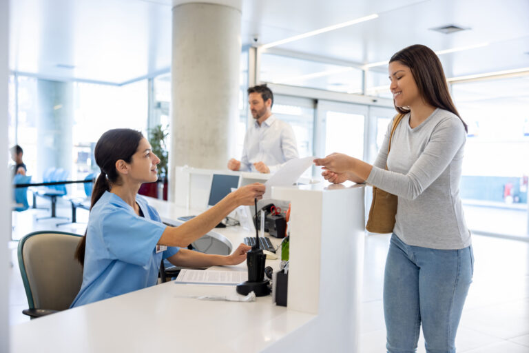 Happy Latin American patient at the hospital handing a form to a nurse at the reception